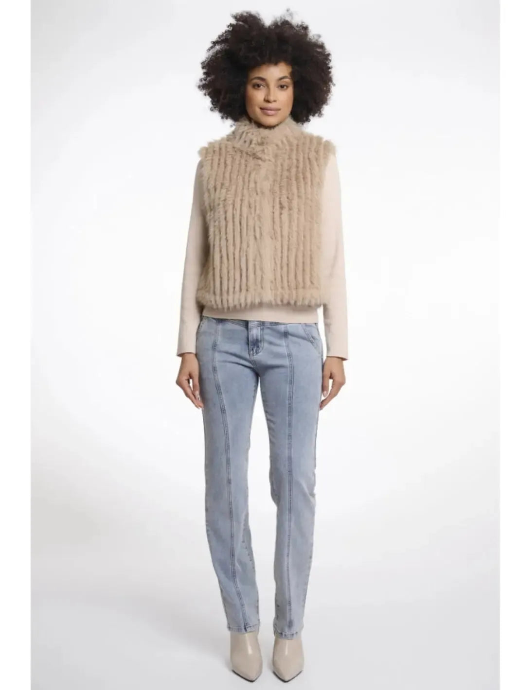 Woman wearing a beige knitted vest over a light shirt with blue jeans on a white background