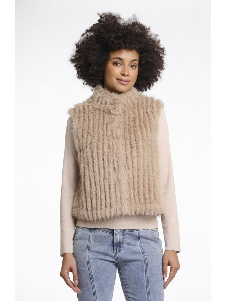 Woman wearing a beige knitted vest over a light sweater with blue jeans on a white background