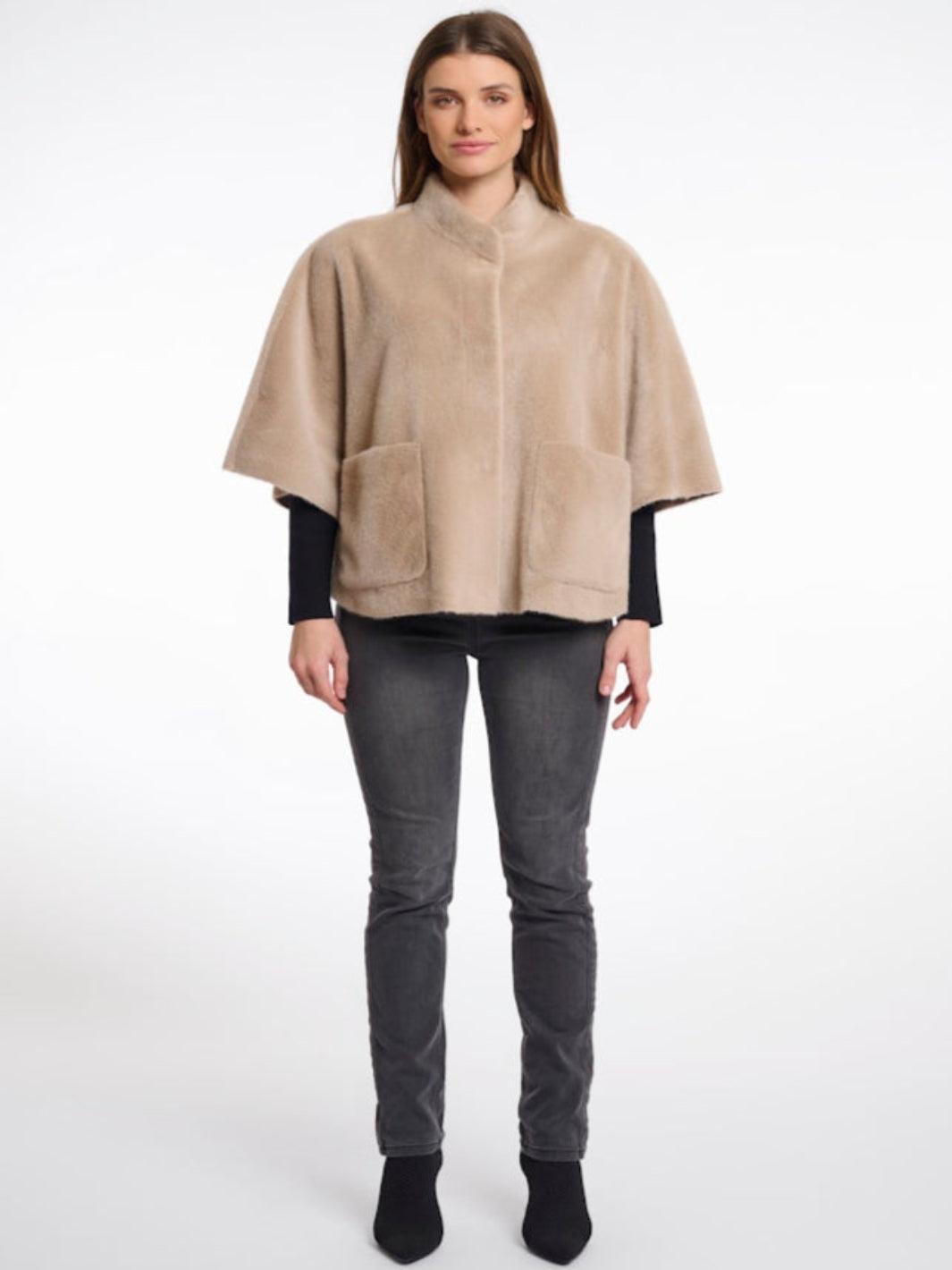 Woman wearing a beige cape over a black top and gray pants on a white background