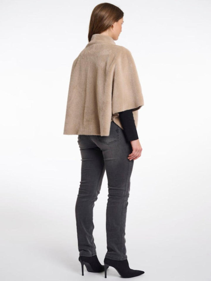 Woman wearing a beige cape over a black top and gray pants on a white background