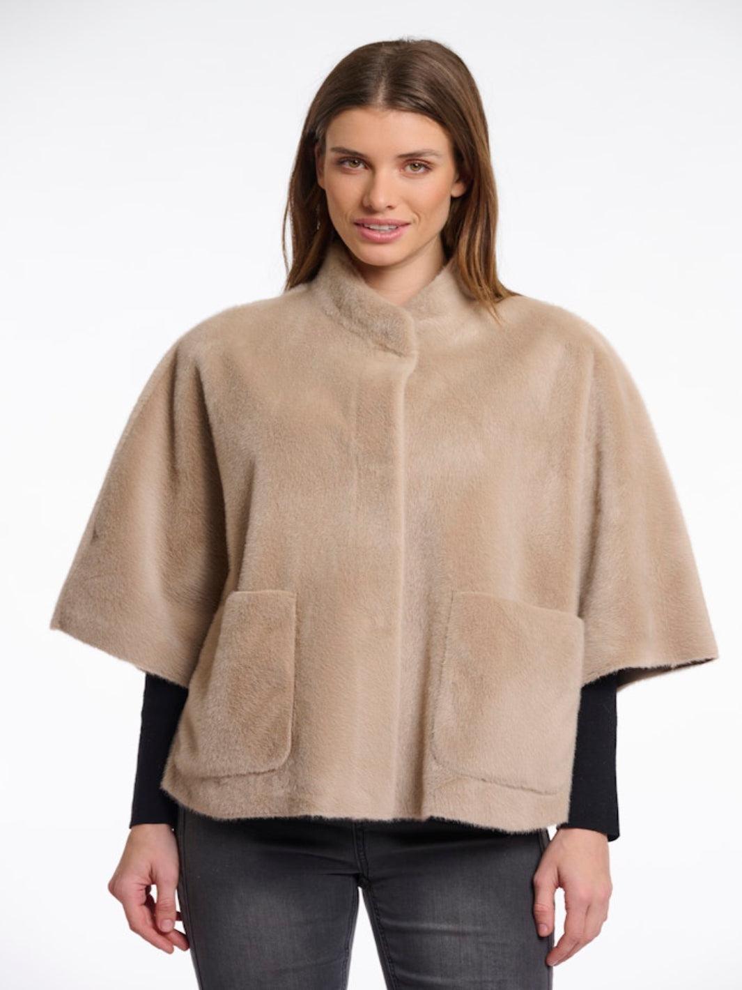 Woman wearing a beige cape over a black top on a white background