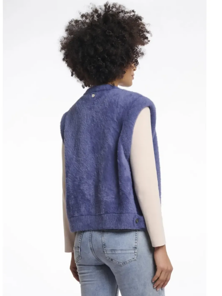 Person wearing a blue denim vest over a white shirt and jeans on a white background