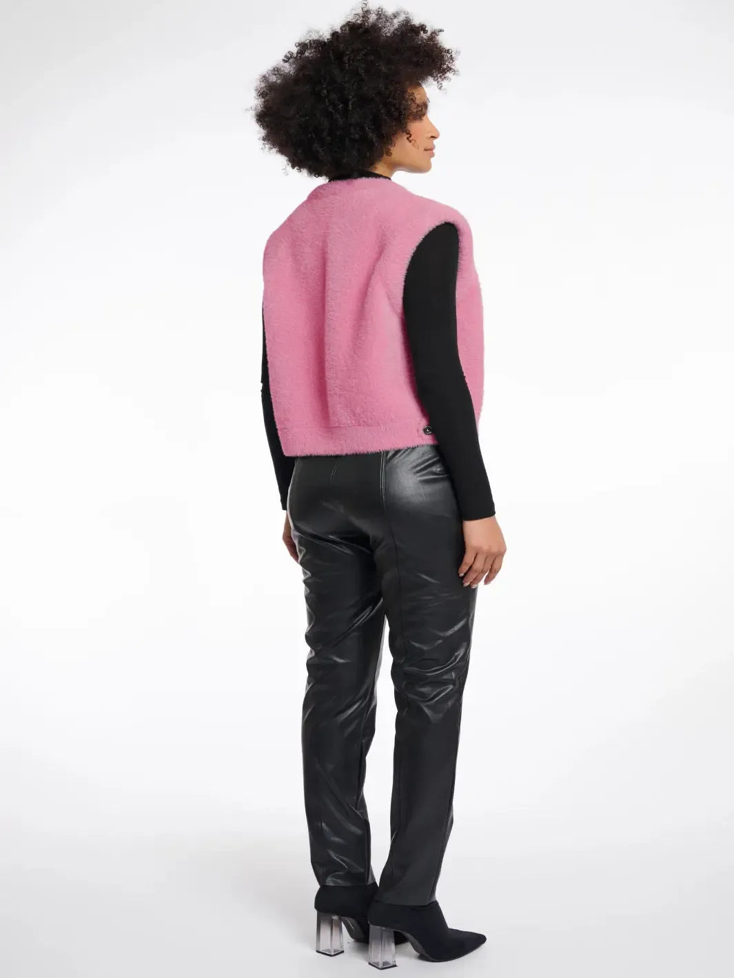 Person wearing a pink vest over a black long-sleeve shirt and black leather pants on a white background