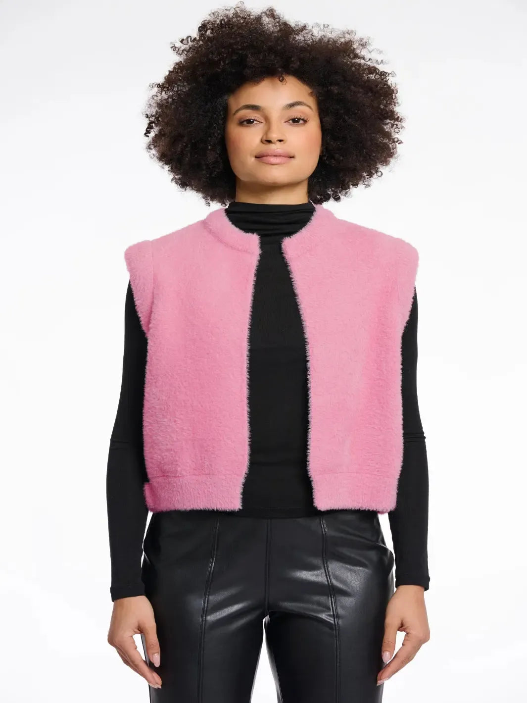 Person wearing a pink vest over a black top and leather pants on a white background