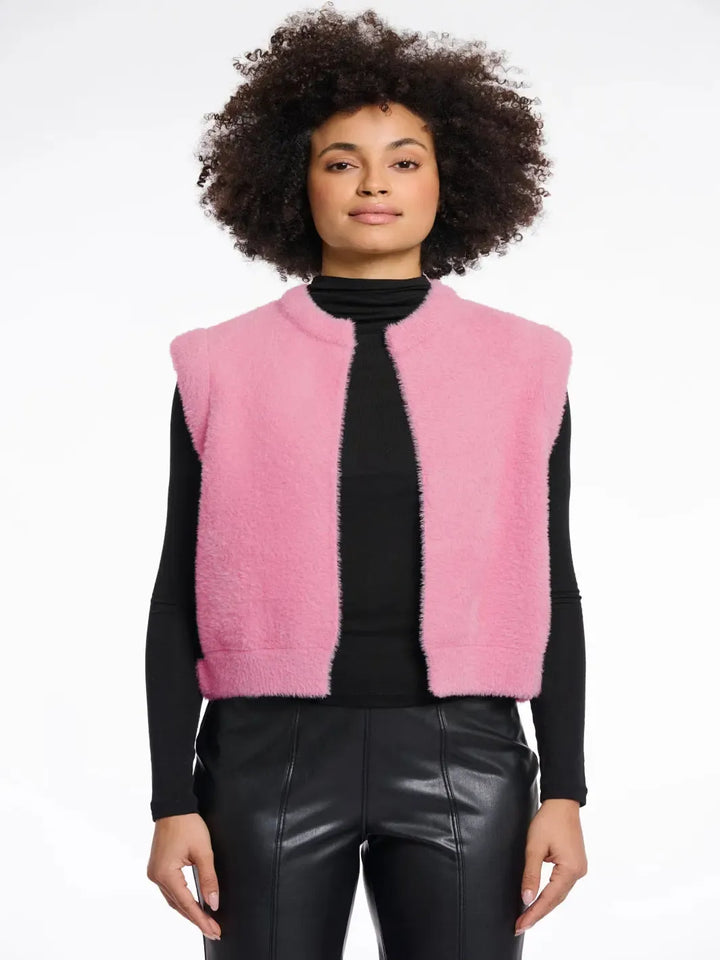 Person wearing a pink vest over a black top and leather pants on a white background