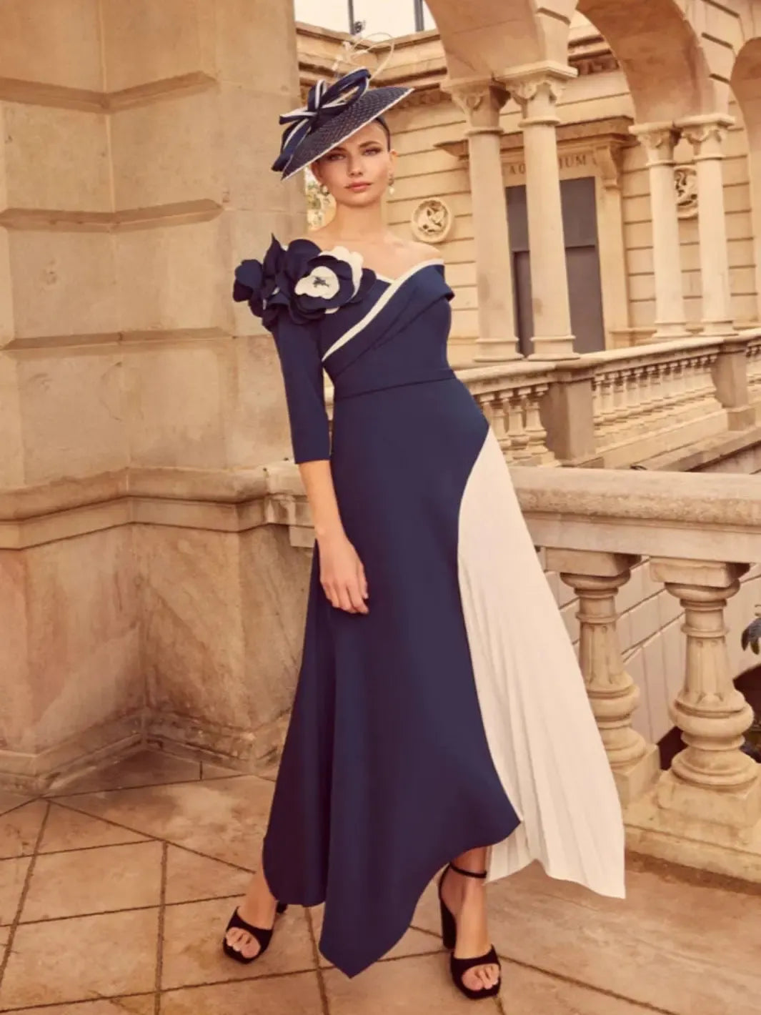 Woman in a navy and white dress with floral details standing in front of an architectural building.