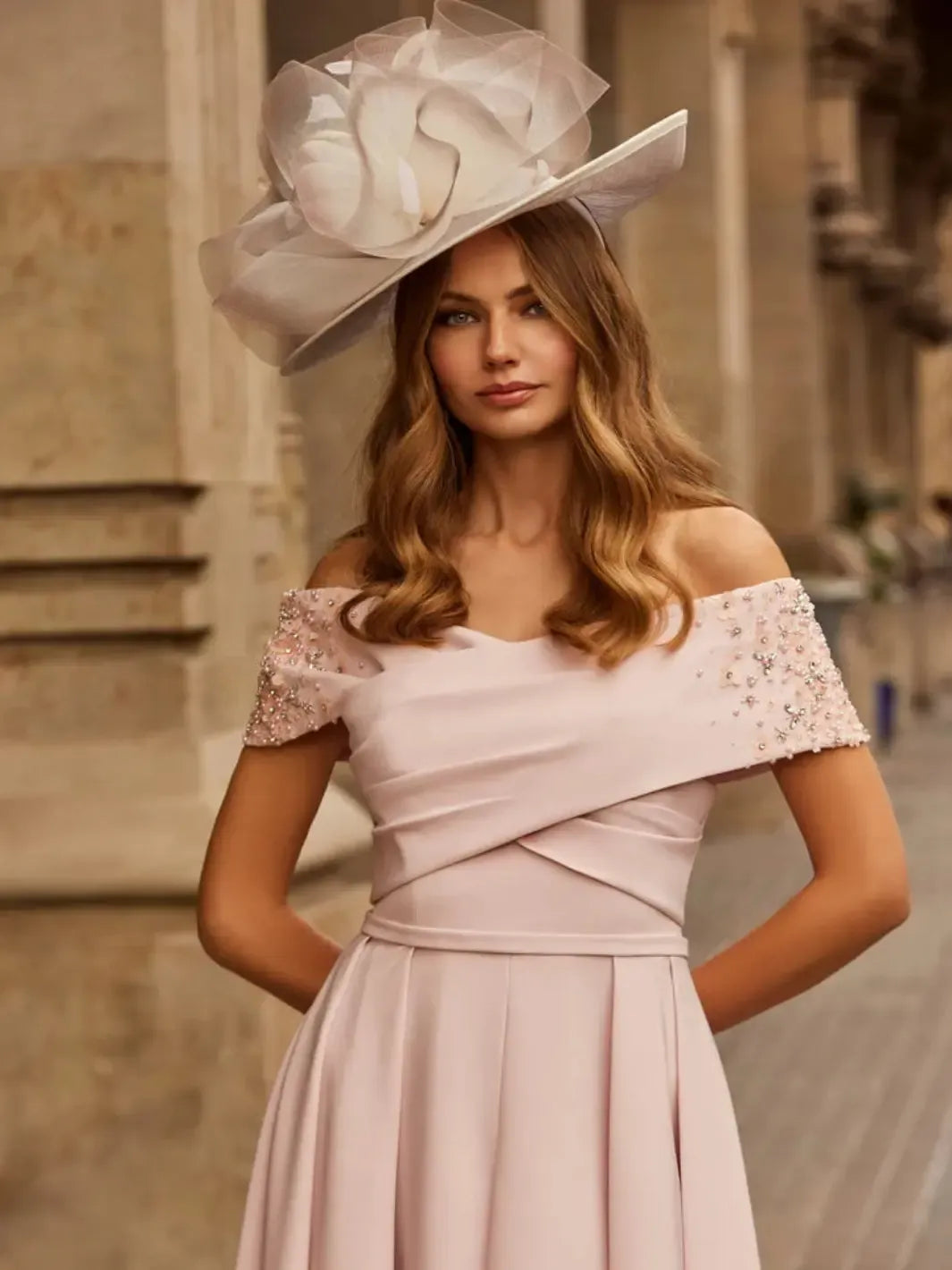Woman wearing a light pink off-shoulder dress with floral embellishments and a large decorative hat.