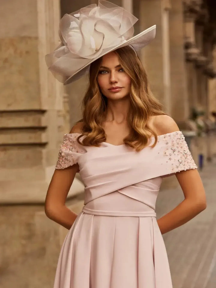 Woman wearing a light pink off-shoulder dress with floral embellishments and a large decorative hat.