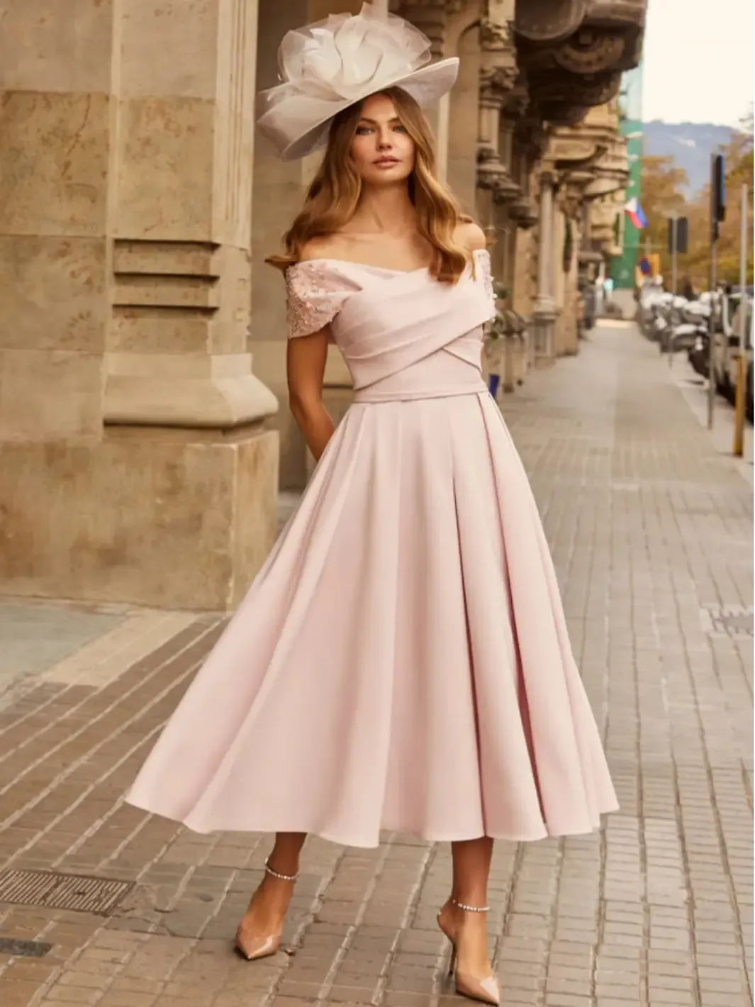 Woman in a pink dress and hat standing on a city street.